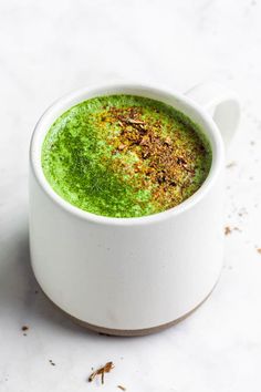 a cup filled with green liquid on top of a white table