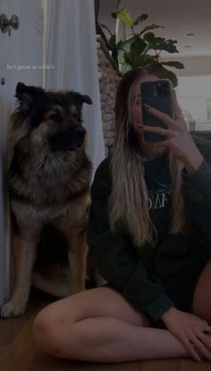 a woman sitting on the floor taking a selfie with her phone next to a dog