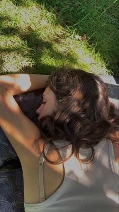 a woman laying in the grass with her back turned to the camera and looking down