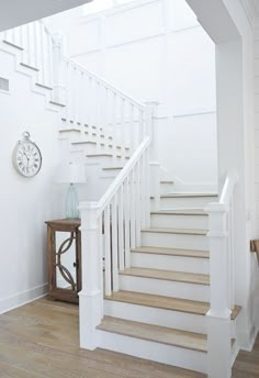 there is a clock on the wall next to some white stairs and railings in this room