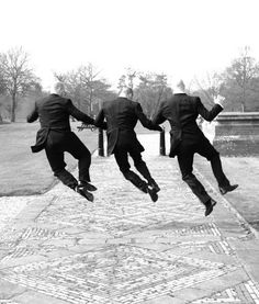 three men in suits jumping up into the air with their legs spread out to catch something