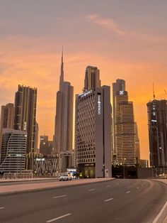 the sun is setting in front of some tall buildings and cars driving down the road