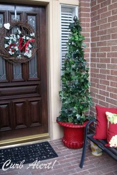 the front door is decorated for christmas with wreaths and potted trees on the porch