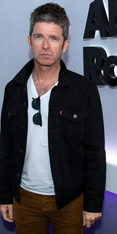 a man in black jacket and white shirt standing next to a blue wall with the words american idol on it