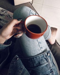 a woman holding a cup of coffee while sitting on a couch with her legs crossed