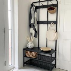 a coat rack with baskets and hats on it in front of a white door next to a black bench