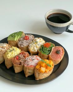 a black plate topped with different types of sushi next to a cup of coffee