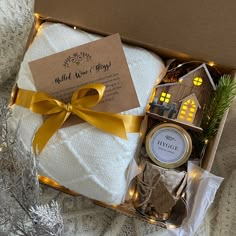 a gift box with white blankets, candles and christmas decorations in it on top of a blanket