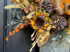 a metal vase filled with lots of different types of flowers and leaves next to a black door