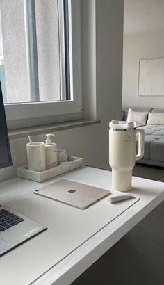 a laptop computer sitting on top of a white desk next to a cup and mug