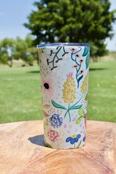 a cup sitting on top of a wooden table next to a green field with trees