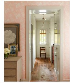 a hallway with pink wallpaper and wooden flooring is seen through an open door