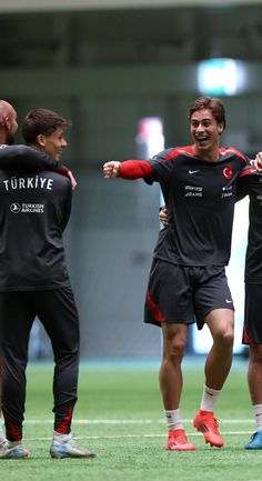 three men in black and red soccer uniforms standing on a field with their arms around each other