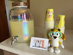 a table topped with lots of cups and a stuffed animal next to a jar filled with liquid