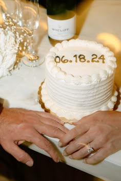 two people holding hands over a wedding cake with the date on it and wine bottles in the background