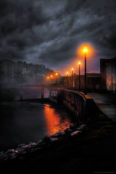 an empty pier at night with lights on and dark clouds in the sky over it