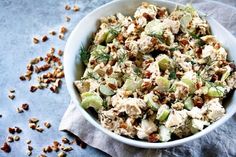 a white bowl filled with chicken salad on top of a blue cloth next to nuts