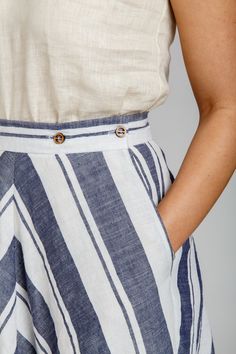 a woman wearing a white top and blue striped skirt with buttons on the waist, standing in front of a gray background