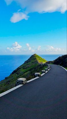 an empty road on the side of a hill with water in the background and blue sky