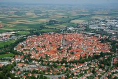 an aerial view of a city with lots of red roofs and green fields in the background