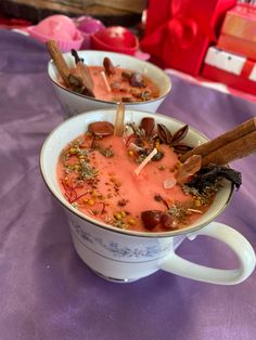 two mugs filled with soup and spices on a purple table cloth covered tablecloth