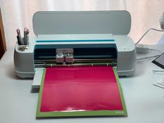 a printer sitting on top of a white desk next to a pink mat and pen