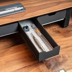 an open drawer with pens and pencils in it on a wooden floor next to a remote control