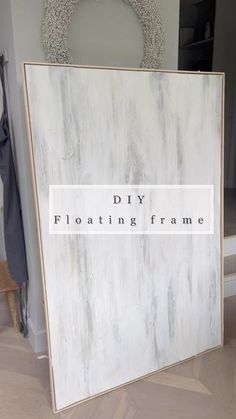 a white frame sitting on top of a hard wood floor next to a wall with a sign that says diy floating frame