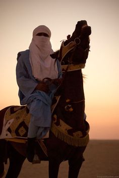 a person riding on the back of a brown horse in the middle of the desert