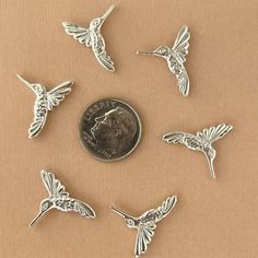 six hummingbird charms sitting on top of a coin next to each other, all in different shapes and sizes