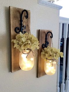 two mason jar lights are hanging on the wall with flowers in them and one light is turned on