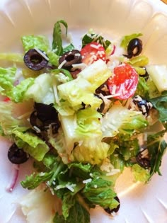 a salad with olives, tomatoes and lettuce on a white paper plate