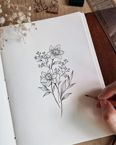 a person is drawing flowers on paper with a pencil and watercolor pen in front of them