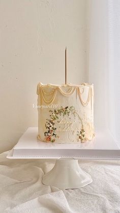 a white cake sitting on top of a white table next to a curtained window