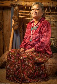 an old woman sitting on the floor in front of some bamboo poles and other items