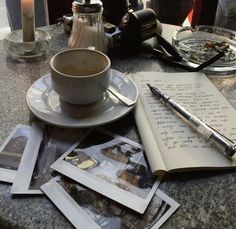 an open book, coffee cup and pen are on a table with other items in front of it