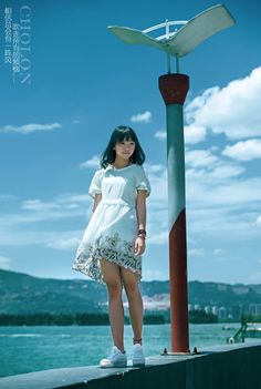 a woman standing on top of a pier next to a pole with a wind vane