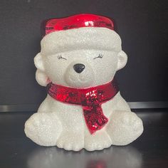 a white teddy bear with a red hat and scarf on it's head sitting on a table