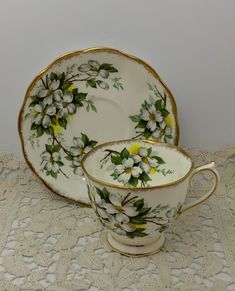 an antique tea cup and saucer decorated with white flowers on a lace tablecloth