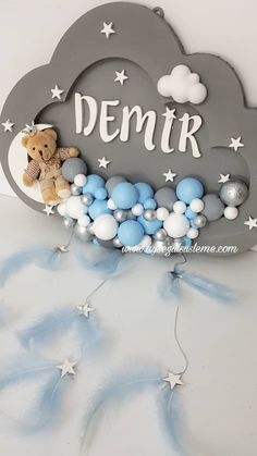 a teddy bear sitting on top of a cloud shaped sign that says demr with blue and white balloons