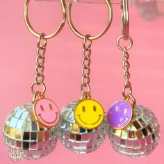 three disco ball keychains with smiley faces on them hanging from a metal hook