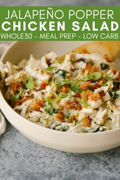 a white bowl filled with chicken salad next to a wooden spoon on top of a table