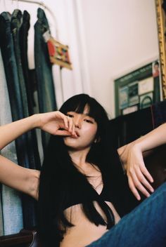 a woman sitting on top of a chair in front of a rack of clothes and holding her hand up to her face