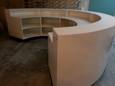 a curved white counter with shelves in the middle and an empty shelf behind it on concrete flooring