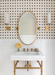 a white sink sitting under a mirror next to a gold faucet and wall mounted lights