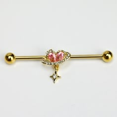 a gold bar with a heart shaped pink stone on it and two balls around the bar