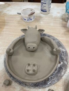 a clay cow is sitting in the middle of a bowl that's made out of cement