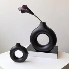 a black vase with a flower in it on a white table next to a book