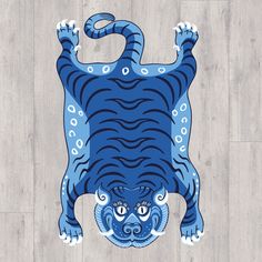 a blue and white tiger on a wood floor with its eyes open, it's body stretched out to the side