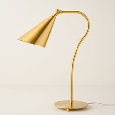 a gold desk lamp on a white surface with a cord plugged into the base